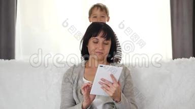 一个女人在家里用平板电脑工作。 小男孩玩捉迷藏，闭上妈妈`<strong>眼睛</strong>，惊喜。 <strong>母亲</strong>和儿子